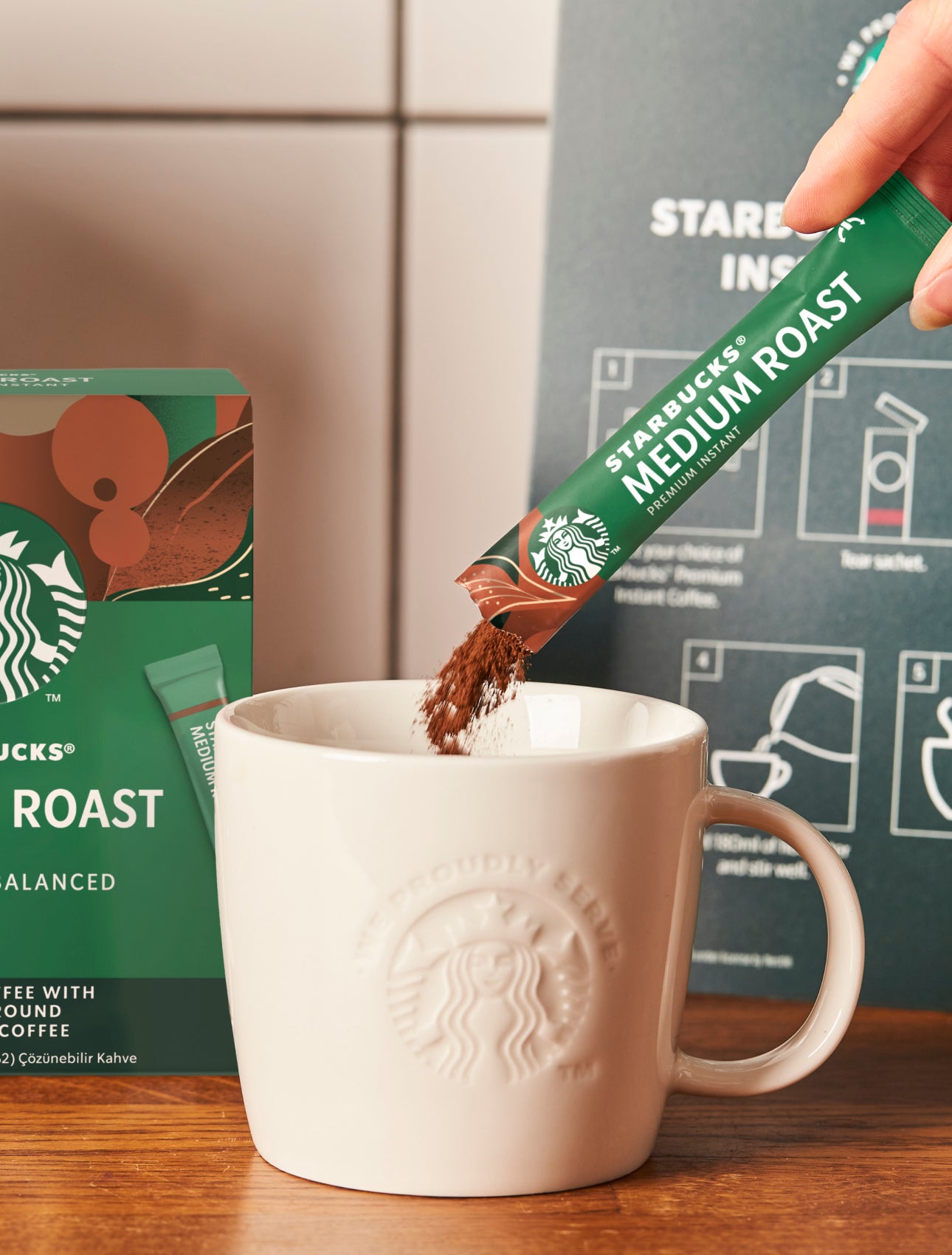一包星巴克優質即溶中度烘焙咖啡倒入印有 We Proudly Serve Starbucks® 星巴克咖啡服務字樣的陶瓷馬克杯中