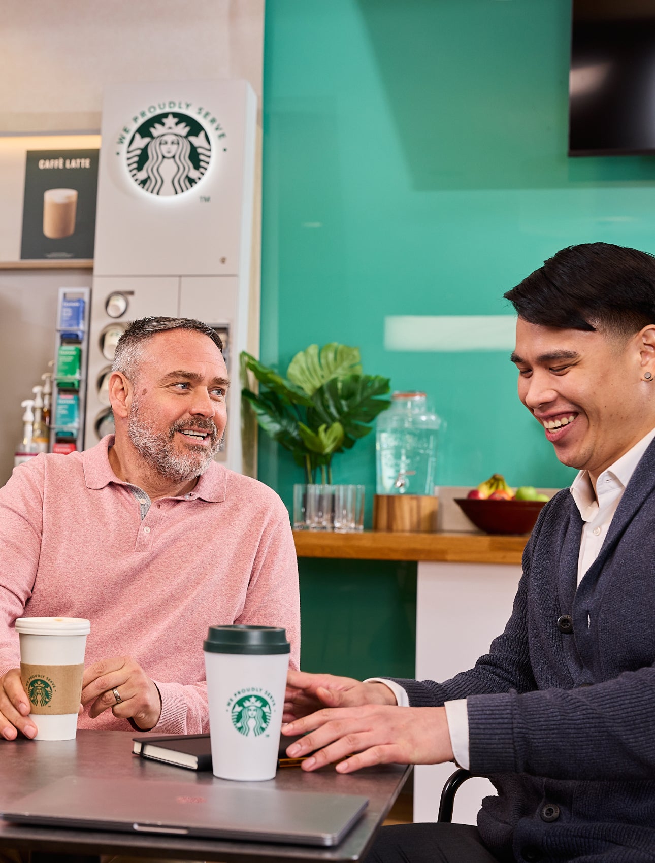 同事們坐在一起，背景中可以看到印有 We Proudly Serve Starbucks 星巴克咖啡服務字樣的杯子和自助咖啡機