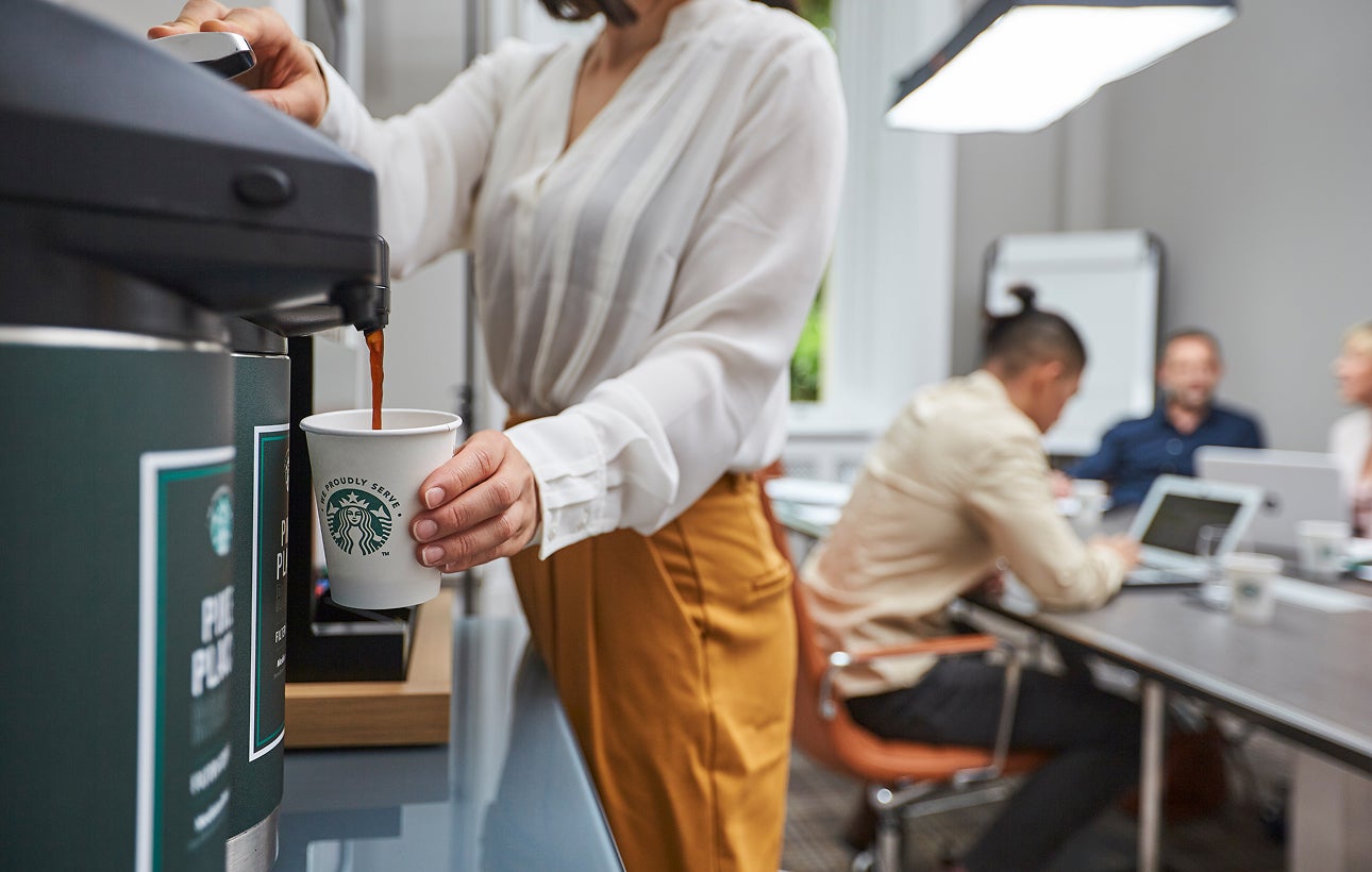 一個人將商用咖啡機煮好的咖啡倒入印有 We Proudly Serve Starbucks 星巴克咖啡服務字樣的紙杯中