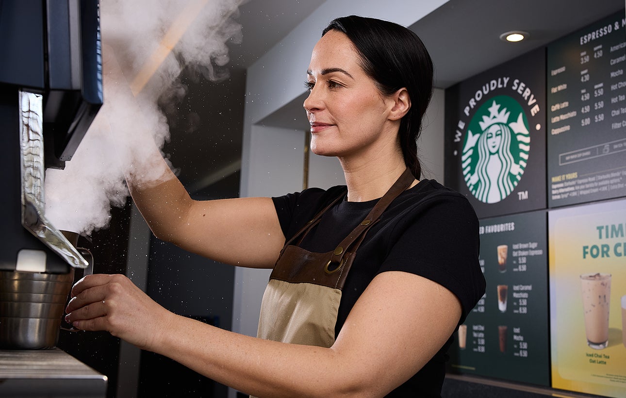 咖啡師為一杯印有 We Proudly Serve Starbucks 星巴克咖啡服務字樣、混合著奶油和咖啡的冰咖啡放上蓋子