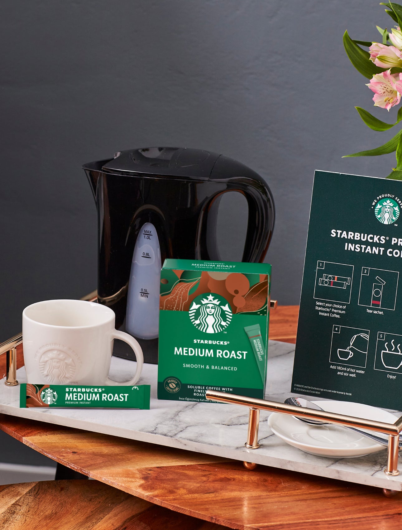 桌面上擺著印有 We Proudly Serve Starbucks 星巴克咖啡服務字樣的馬克杯、星巴克即溶咖啡和沖泡說明
