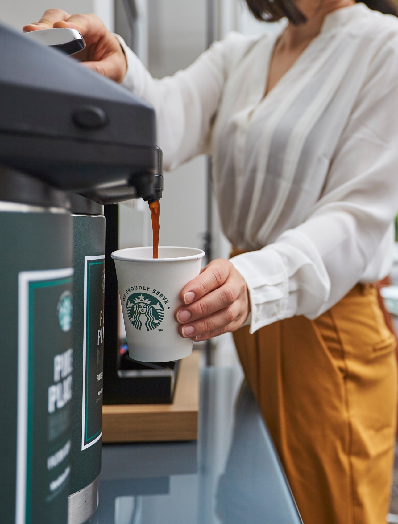 一個人將商用咖啡機煮好的咖啡倒入印有 We Proudly Serve Starbucks 星巴克咖啡服務字樣的紙杯中