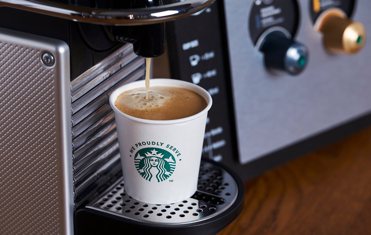 一個印有 We Proudly Serve Starbucks 星巴克咖啡服務字樣的紙杯裝滿由濃縮咖啡機新鮮沖泡的咖啡
