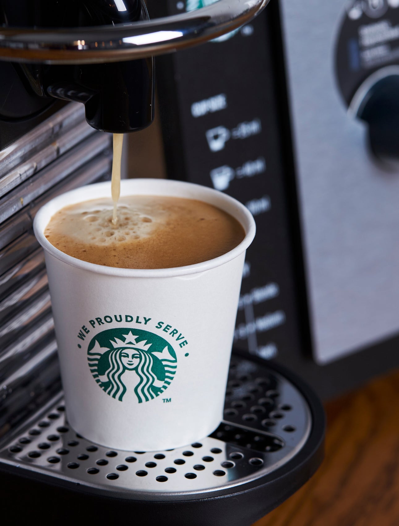 一個印有 We Proudly Serve Starbucks 星巴克咖啡服務字樣的紙杯裝滿由濃縮咖啡機新鮮沖泡的咖啡