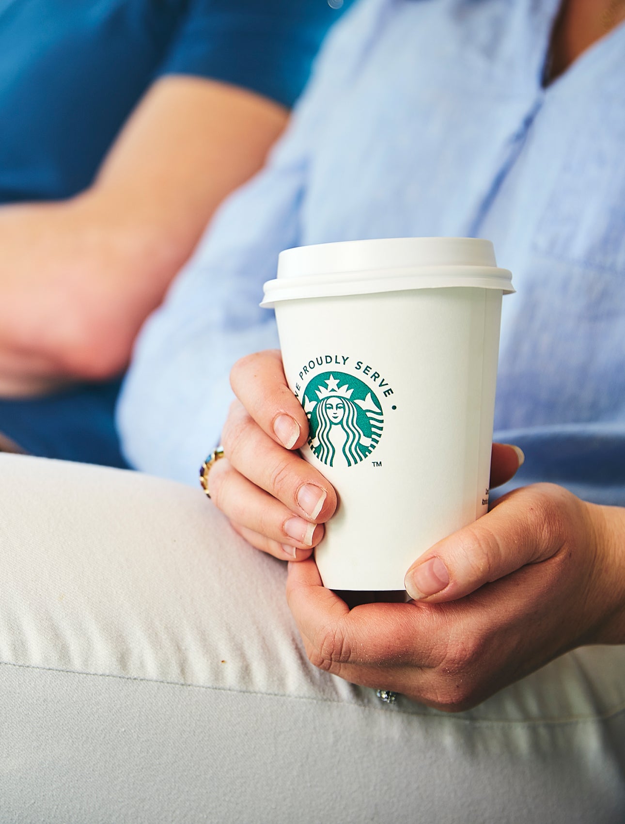 一個人坐著,雙手拿著一個印有 We Proudly Serve Starbucks 星巴克咖啡服務字樣的外帶杯
