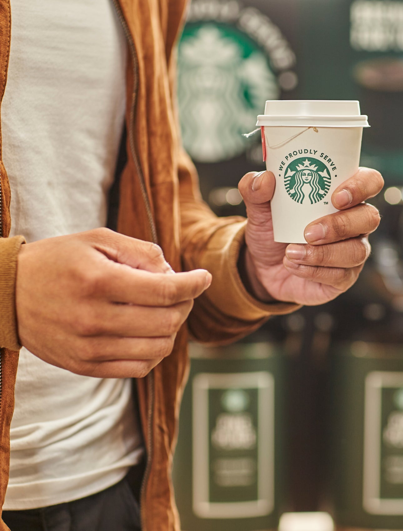 一個人手裡拿著一杯茶，杯子上印著 We Proudly Serve Starbucks 星巴克咖啡服務字樣