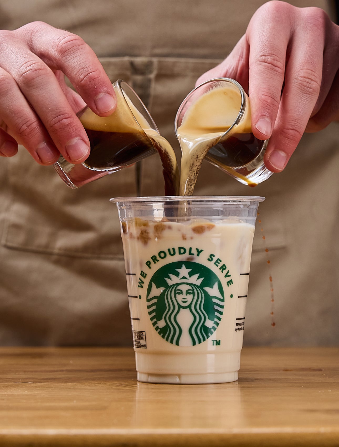 咖啡師同時將兩份濃縮咖啡倒入印有 We Proudly Serve Starbucks 星巴克咖啡服務字樣的杯子中,杯子裡裝了冰塊和牛奶