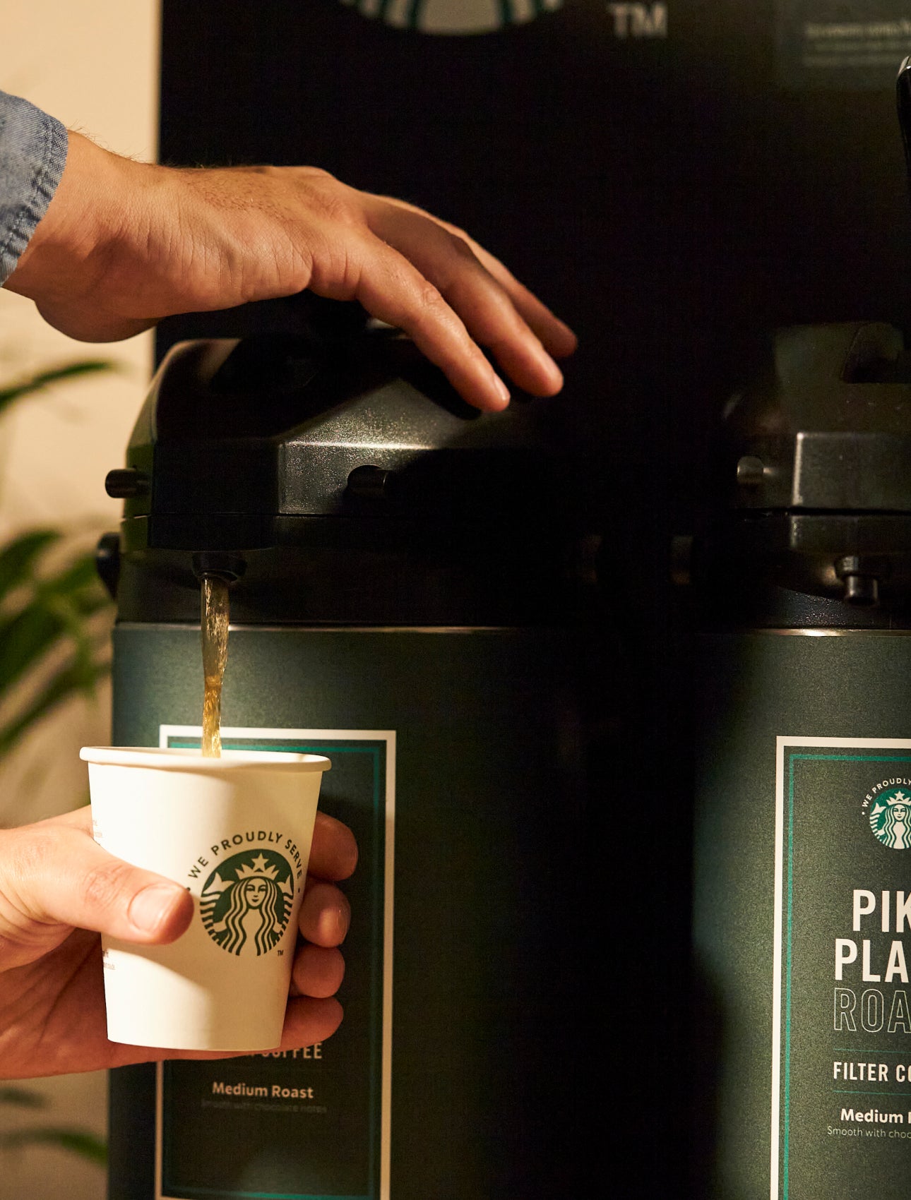 一個人從大型咖啡機將星巴克 Pike Place™ 派克市場烘焙咖啡倒入印有 We Proudly Serve Starbucks® 星巴克咖啡服務字樣的杯子中