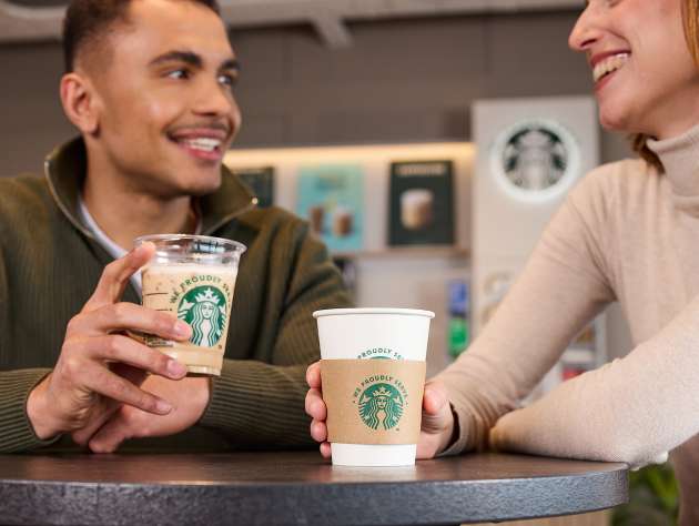 咖啡館裡，兩個人拿著印有 We Proudly Serve Starbucks 星巴克咖啡服務字樣的飲品