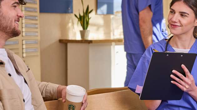 一位身穿藍色手術服的女士在診所內與一位手持印有 We Proudly Serve Starbucks 星巴克咖啡服務字樣的咖啡杯的患者交談。